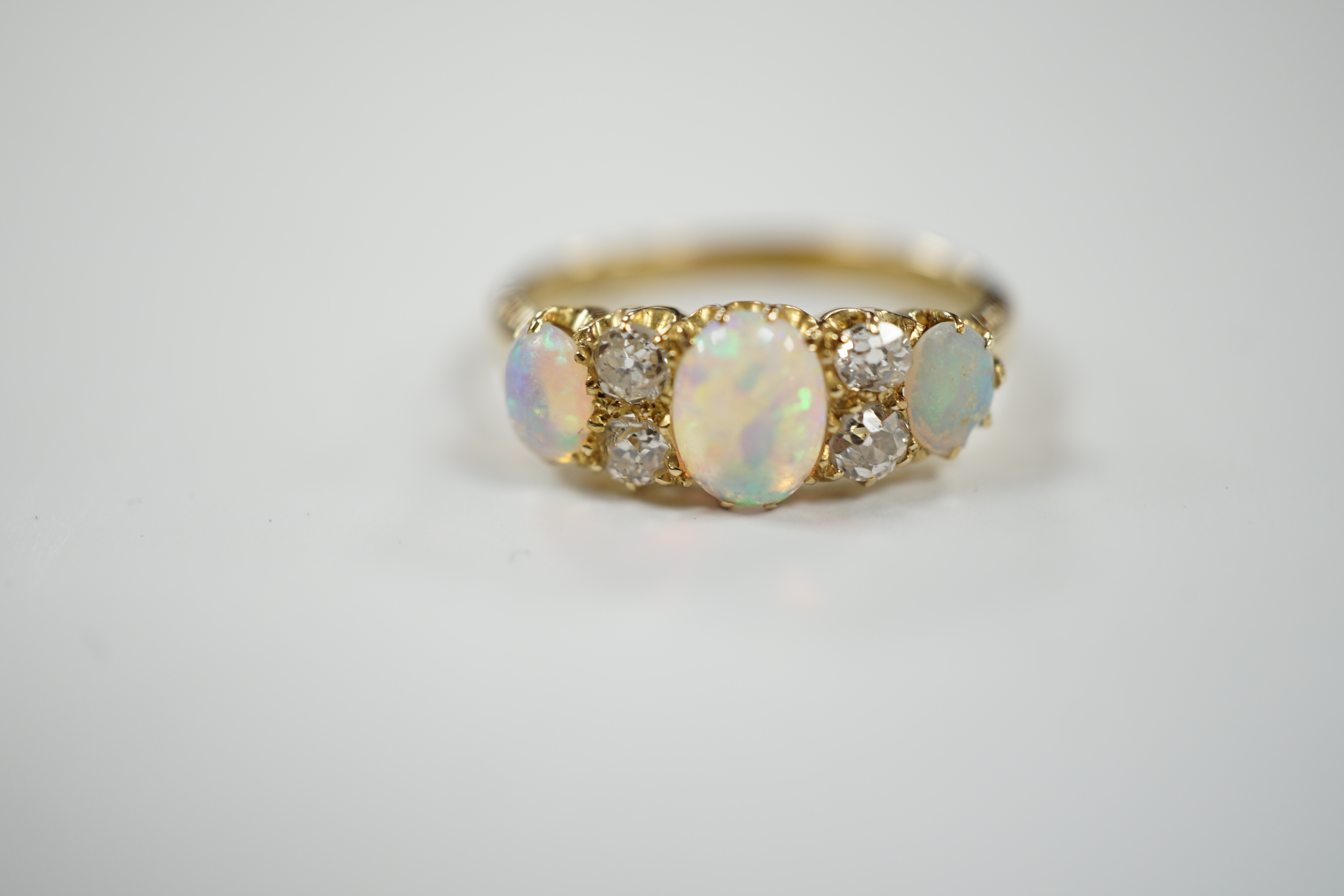 A yellow metal (tests as 18ct), three stone white opal and four stone diamond set half hoop ring, size N/O, gross weight 3.5 grams.